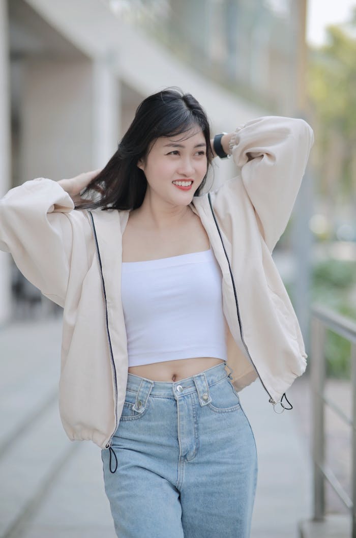 Asian woman in a casual outfit, smiling while walking outdoors in an urban setting, showcasing a relaxed style.