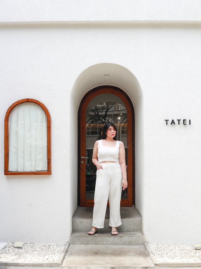 Young woman in white attire standing at a minimalist architectural entrance with arched door.